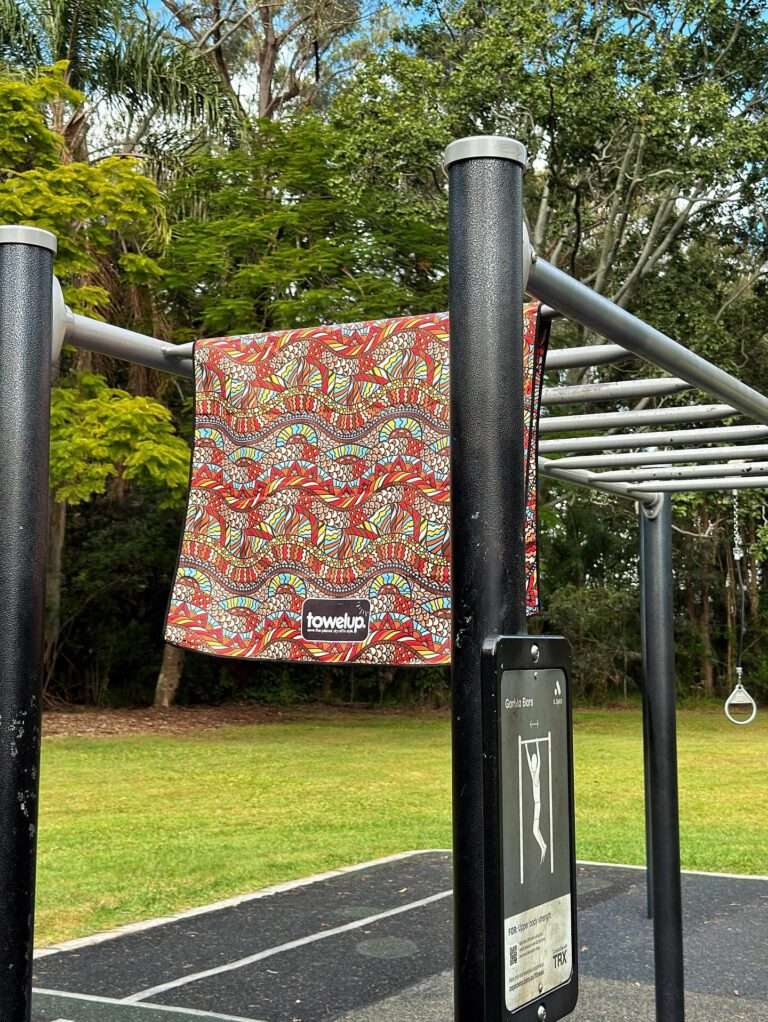 Various gym towels from the brand 'towelup.' hanging up in a park outside. Backdrop of nature and trees.