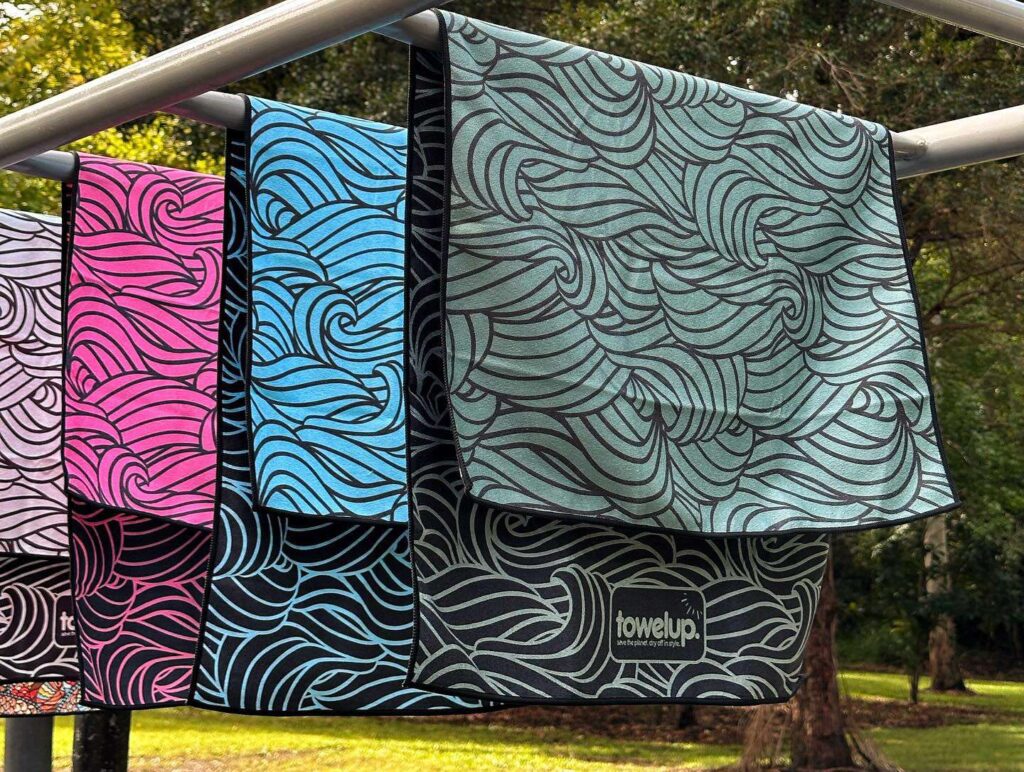 Various gym towels from the brand 'towelup.' hanging up in a park outside. Backdrop of nature and trees.